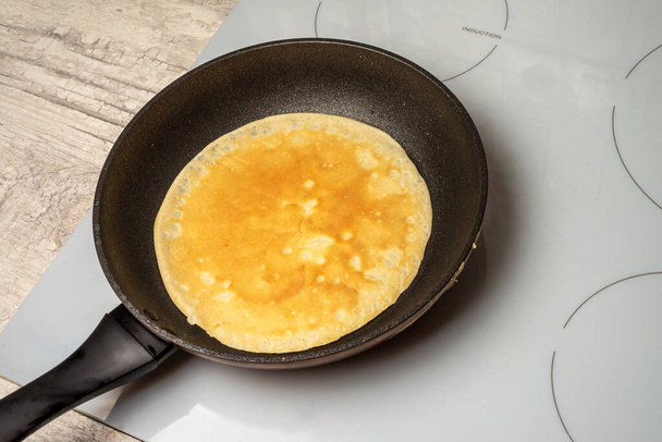 Pannenkoek wordt gebakken in een pan op een inductiekookplaat. - Foto, afbeelding
