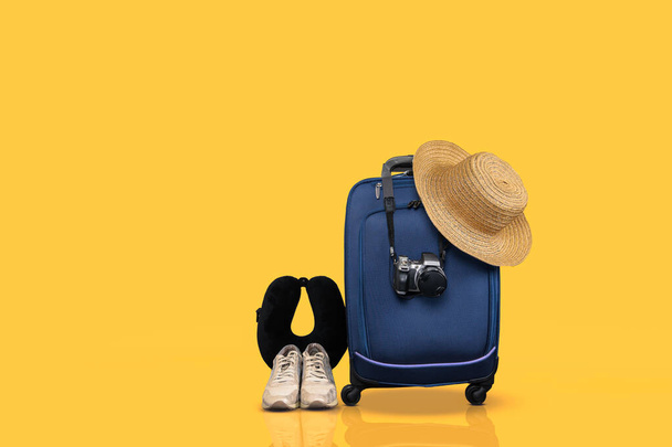 Kék kerekű kézipoggyász és alapvető utazási cikkek sárga háttér mellett. - Fotó, kép