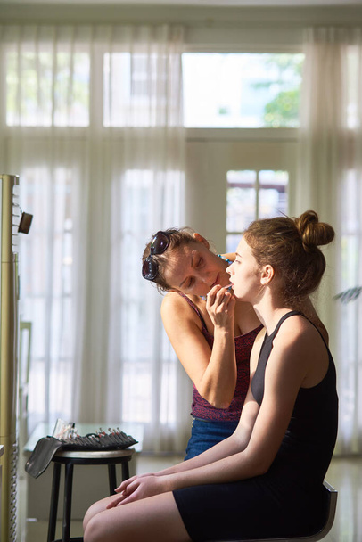 Maquillaje profesional artista forro labios de mujer joven y bonita sentada en el taburete delante del espejo - Foto, Imagen