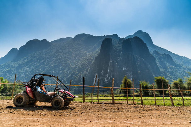 Женщина водит грязную коляску в сельскую дикую местность Азии и парков, чтобы полюбоваться впечатляющим горным фоном. Припаркован на грунтовой дороге вдоль пастбища. - Фото, изображение