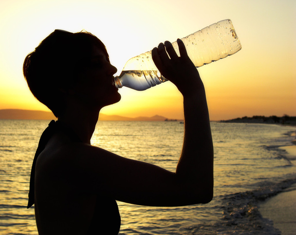 ビーチで水を飲む女性のシルエット - 写真・画像