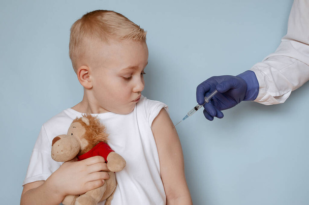Doctor vaccinates a cute little boy from Covid-19 on a blue background, close-up. - Foto, Imagen