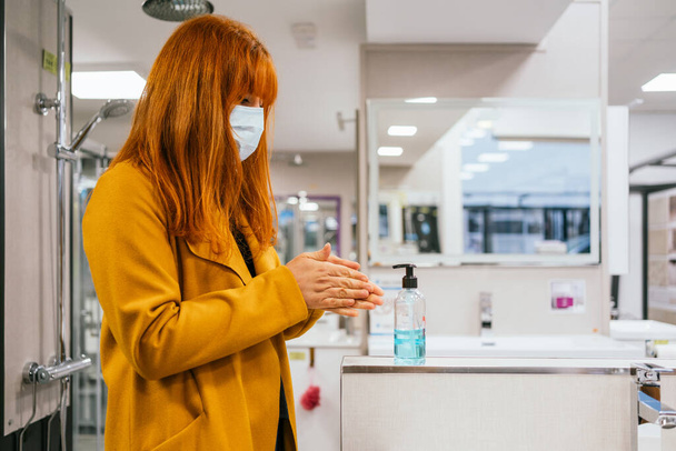 A blonde Spanish woman wearing a face mask applying hand sanitize - Foto, imagen