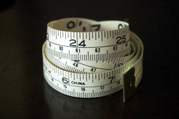 Rolled measuring tape on a semi-reflective dark surface - Photo, Image