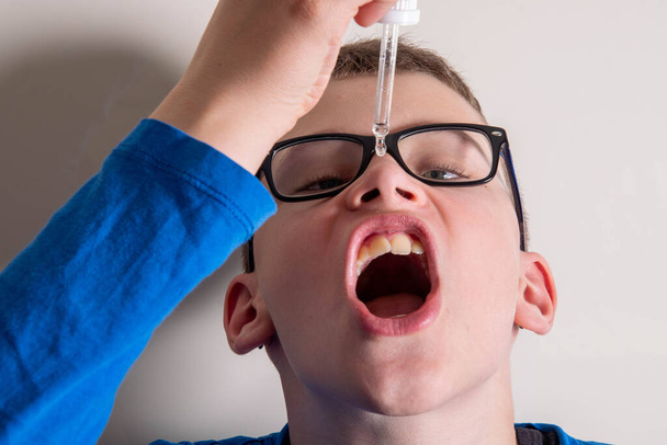 Child with glasses drips medicine from pipette into mouth - Photo, Image