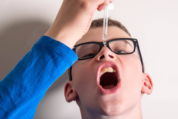 Dziecko w okularach kapie lek z pipety do ust - Zdjęcie, obraz
