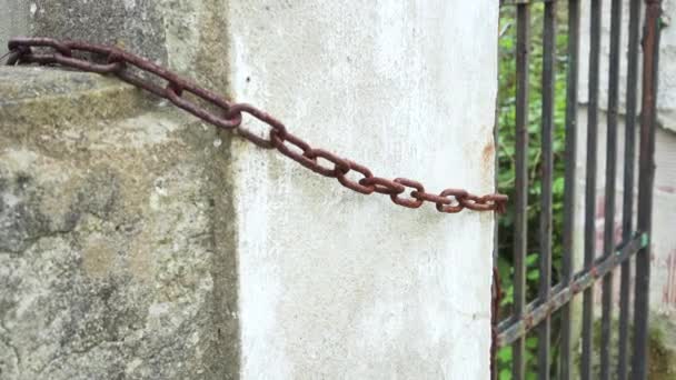 Antigua cadena oxidada en una valla de hormigón de una casa abandonada con una puerta de celosía - Imágenes, Vídeo