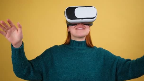 Εντυπωσιασμένη νεαρή γυναίκα που χρησιμοποιεί κράνος VR app headset για να παίξει παιχνίδι προσομοίωσης, σχέδιο. Παρατηρώντας εικονική πραγματικότητα 3d 360 βίντεο. Απομονωμένο σε κίτρινο φόντο στο στούντιο. - Πλάνα, βίντεο