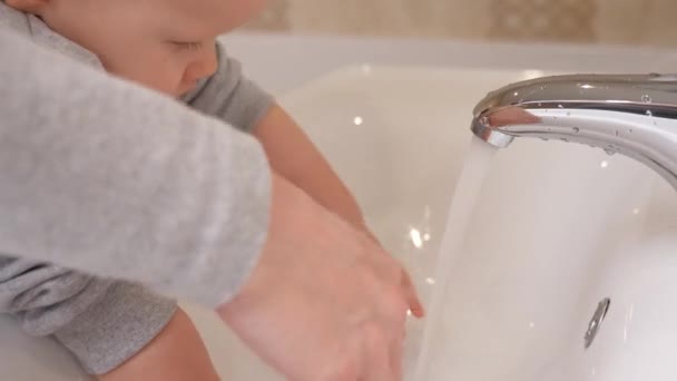 Un bambino piccolo si lava le mani con sua madre nel bagno sopra il lavandino. Una madre aiuta suo figlio a lavarsi le mani a casa. Il ragazzo impara a lavarsi le mani da solo. Giochi l'acqua con il bambino. - Filmati, video