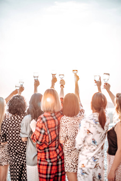 Group of female friends celebrate and rise their hands up holding wineglasses - Photo, Image
