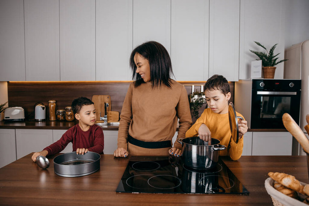 Heureuse mère de famille afro-américaine et deux fils qui s'amusent à cuisiner le déjeuner dans la cuisine - Photo, image