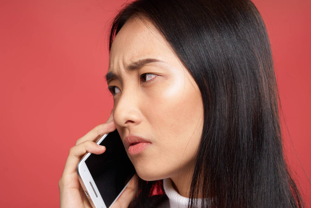 woman of asian appearance talking on the phone emotions dissatisfaction close-up red background - Foto, afbeelding