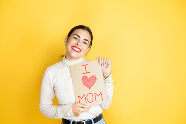 Hermosa mujer celebrando el día de las madres sosteniendo el cartel de amor mensaje de mamá con una cara feliz de pie y sonriendo con una sonrisa confiada mostrando los dientes - Foto, imagen