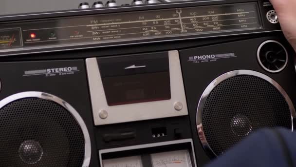 Varón sostiene grabadora de cinta de audio vintage en las manos con cassette de audio giratorio - Imágenes, Vídeo