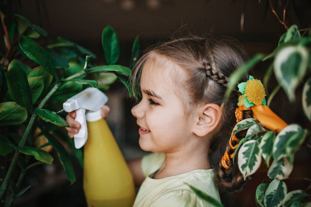 Aranyos lány segít, hogy vigyázzon a hazai növények az ablakon, növény szülők koncepció - Fotó, kép