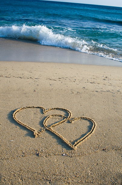 Dois corações esculpidos desenhados na areia de uma praia
 - Foto, Imagem