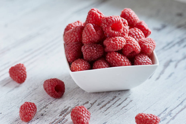 Close-up photo of raspberries in a white bowl on a white wooden table. - Photo, Image