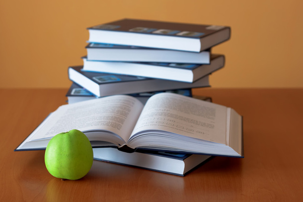 Зеленое яблоко и открытые книги на столе
 - Фото, изображение