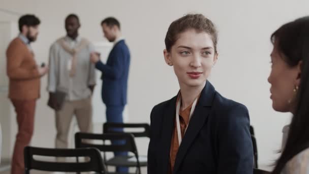 Chest-up of young Caucasian businesswoman communicating with cropped colleague in conference room, smiling - Footage, Video