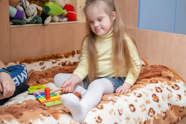 Egy Down-szindrómás gyermek harmonikus fejlődése. Zeneterápia Down-szindrómás gyerekeknek. Egy lány Down-kóros játszik a scylophone az otthonában. - Fotó, kép