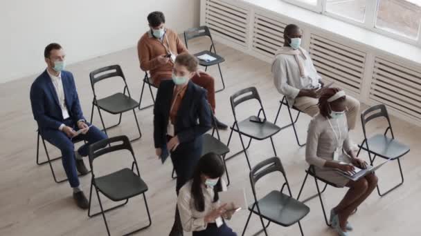 High angle of diverse male and female businesspeople wearing formal clothing and medical face masks, sitting in conference room, keeping social distance, Caucasian woman standing up and leaving - Footage, Video