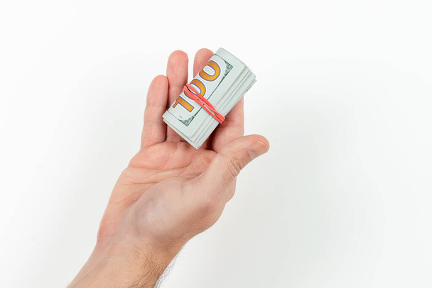 Un homme tient dans sa main de l'argent dans un rouleau attaché avec une bande isolée sur un fond blanc. Monnaie dollar américain - Photo, image