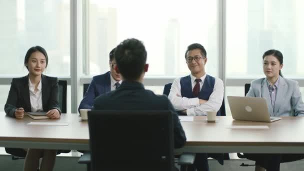 achteraanzicht van een jonge Aziatische zakenman die wordt geïnterviewd door een groep HR-leidinggevenden in een conferentieruimte van een modern bedrijf - Video