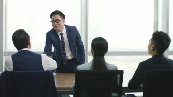 nuori aasialainen liikemies työnhakija kättelee ja tervehtii ryhmää henkilöstöjohtajia nykyaikaisen yrityksen kokoushuoneessa - Materiaali, video