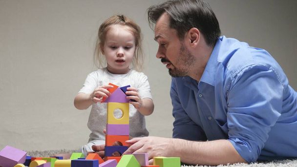 A child, a girl and a dad are building family home. Happy family. Educational games for children. Father and daughter play colorful cubes in nursery on floor. Teaching child through play activities - Photo, Image