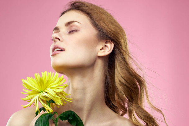 ピンクの背景に黄色の花を持つ女性の肖像｜化粧を顔に - 写真・画像