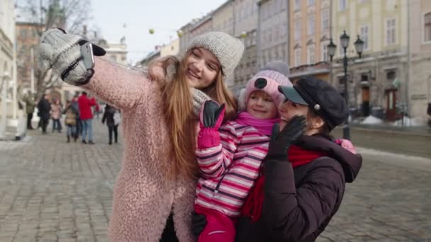 Γυναίκες τουρίστες λήψη selfie φωτογραφίες στο κινητό τηλέφωνο με το κορίτσι υιοθεσία παιδί στο δρόμο της πόλης το χειμώνα - Πλάνα, βίντεο