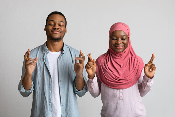 Африканская мусульманская пара с закрытыми глазами и скрещенными пальцами - Фото, изображение