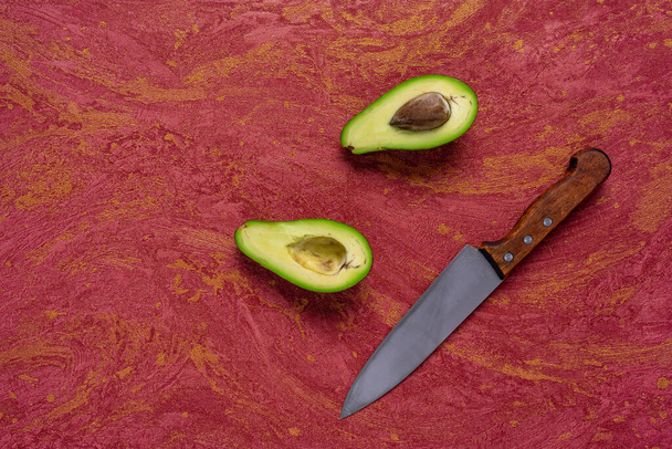 Avocado face. Avocado cut in the middle and knife on red background. varieties avocado top view - Foto, Imagem