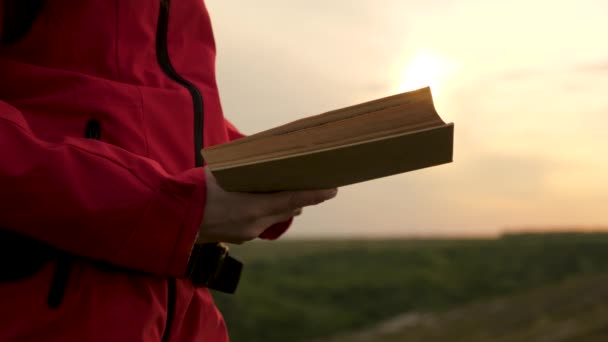 A student reads a textbook in the park outdoors in the rays of the sunset. Young woman traveler reads book at a halt. Girl tourist with a book on the mountain in sun over the river. Prayer in nature. - Footage, Video