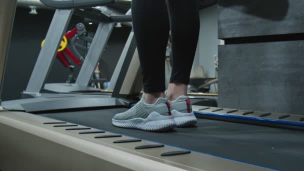 Back down view of woman starts to walk to warn up on treadmill close up - Footage, Video