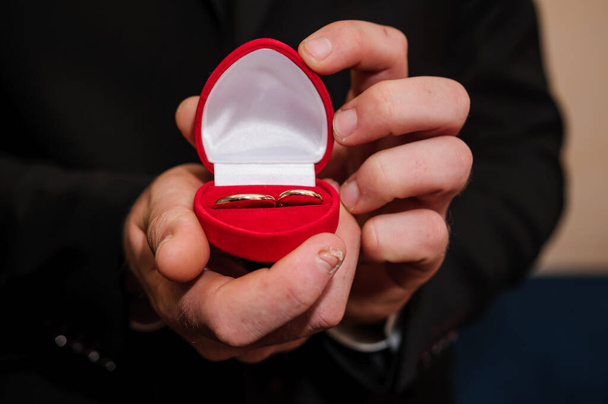 Anelli d'oro nuziale in una scatola rossa, anelli d'oro nuziale nelle mani dello sposo - Foto, immagini