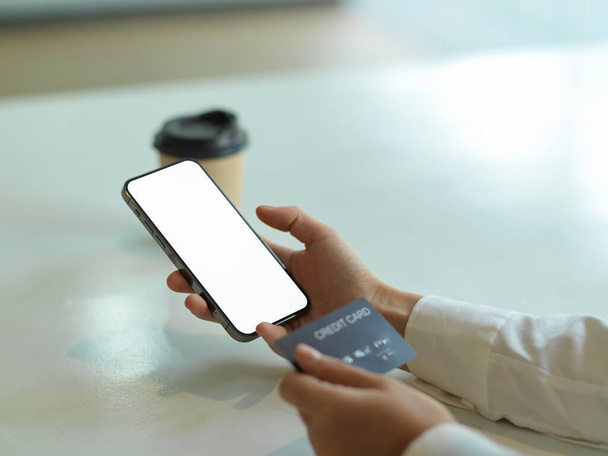Vista de perto da mão usando smartphone com tela de simulação e segurando cartão de crédito, conceito bancário on-line, caminho de recorte - Foto, Imagem