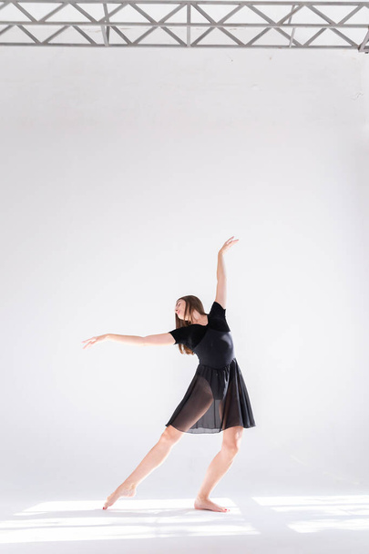 Een slank meisje in een zwarte sportjurk poseert terwijl ze danst op een witte geïsoleerde achtergrond. Meisje atleet dansen op een witte geïsoleerde achtergrond met plaats voor tekst of logo. - Foto, afbeelding