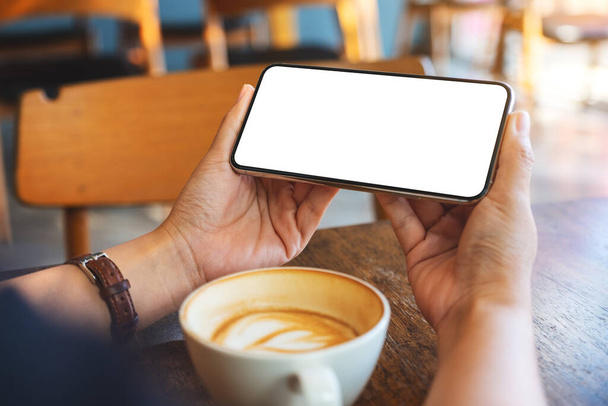 Mockup-Bild einer Frau mit schwarzem Handy mit leerem Bildschirm und Kaffeetasse auf Holztisch - Foto, Bild