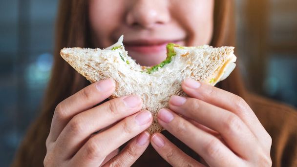 Крупный план красивой женщины, держащей и кусающей сэндвич из цельной пшеницы  - Фото, изображение