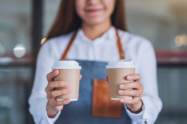 Kelnerka trzymająca i podająca dwie papierowe filiżanki gorącej kawy w kawiarni - Zdjęcie, obraz