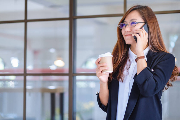 Крупный план деловой женщины, держащей чашку кофе во время разговора по мобильному телефону - Фото, изображение