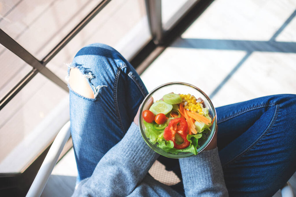 Зображення жінки, що тримає тарілку свіжого змішаного салату з овочами, сидячи на підлозі
 - Фото, зображення