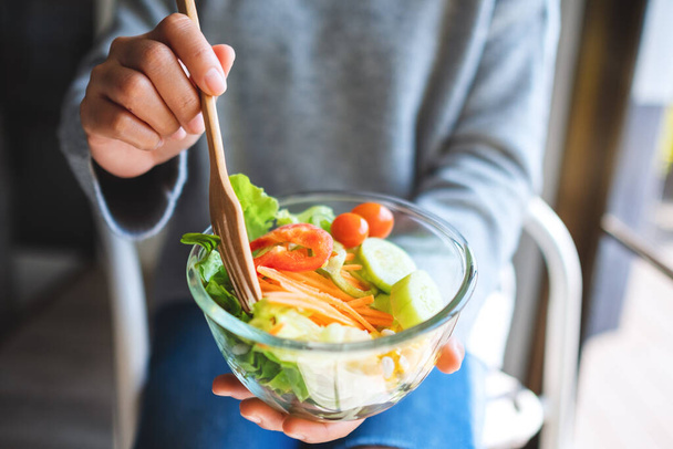 Close-up beeld van een vrouw eten en houden van een kom verse gemengde groenten salade door vork - Foto, afbeelding