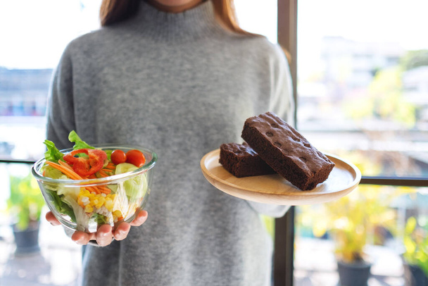Egy nő, aki ételt tart és választ egy tál süti és egy tál zöldség saláta között.  - Fotó, kép