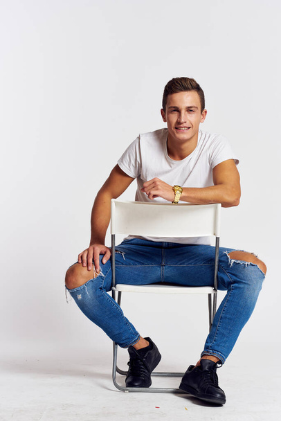 A man in jeans sits on a chair backwards and and ripped jeans T-shirt front view - Photo, Image