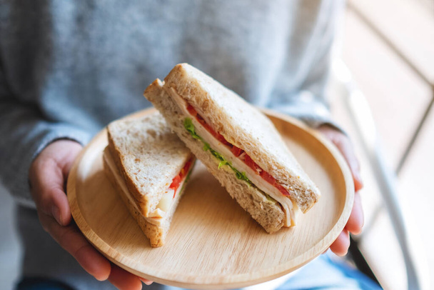 A woman holding two pieces of whole wheat sandwich in wooden plate - Photo, Image