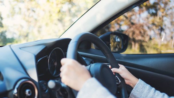 Closeup image of a woman holding steering wheel while driving a car on the road - Photo, Image