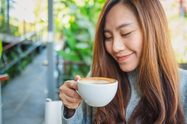 Closeup image of a beautiful asian woman holding a cup of hot coffee to drink - Photo, Image