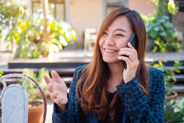 Μια όμορφη Ασιάτισσα μιλάει στο κινητό με χαμογελαστό πρόσωπο στην εξοχή. - Φωτογραφία, εικόνα